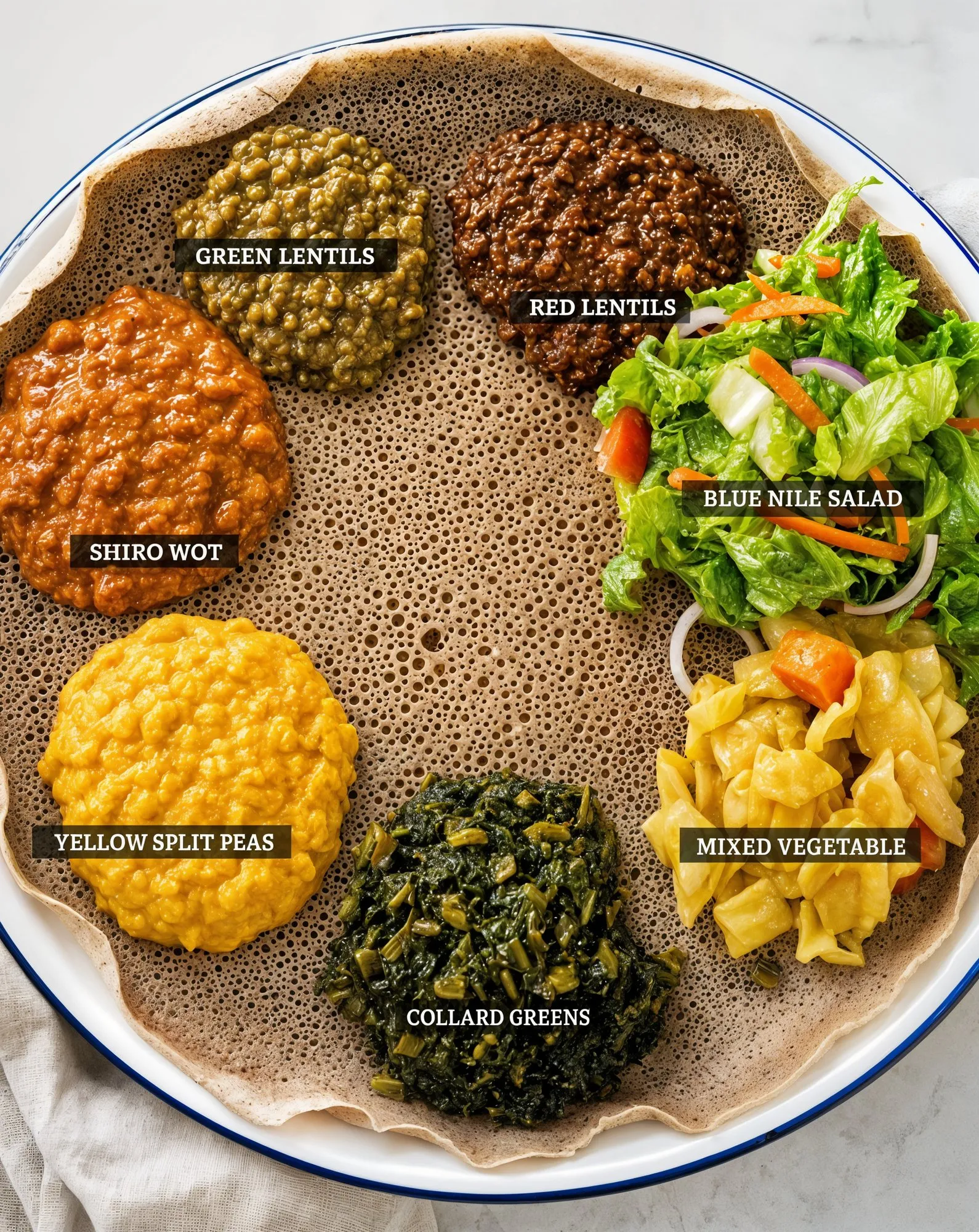 Yetsom Beyaynetu platter with labeled lentils, split peas, collard greens, and salad on injera